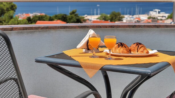 A table with croissants and orange juice, overlooking a coastal view.
