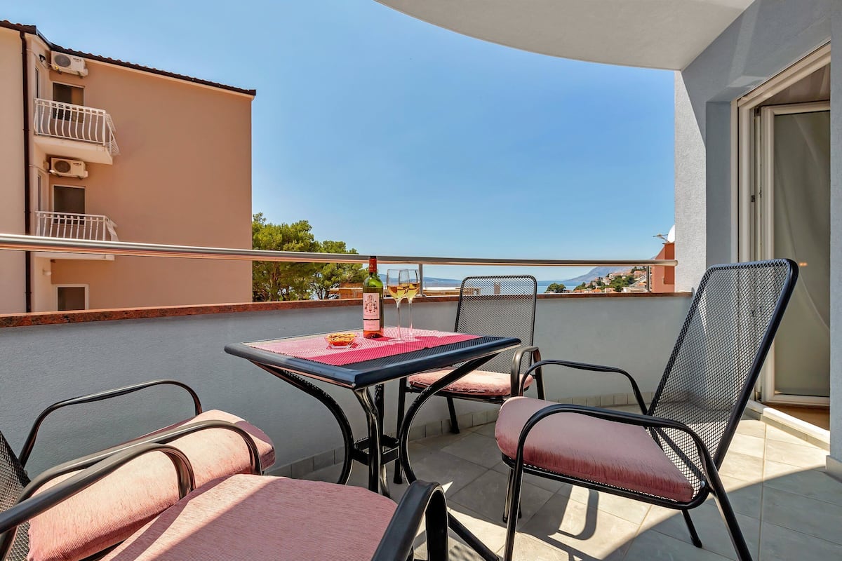 Een balkon met een tafel gedekt voor twee personen, twee stoelen en uitzicht op zee.