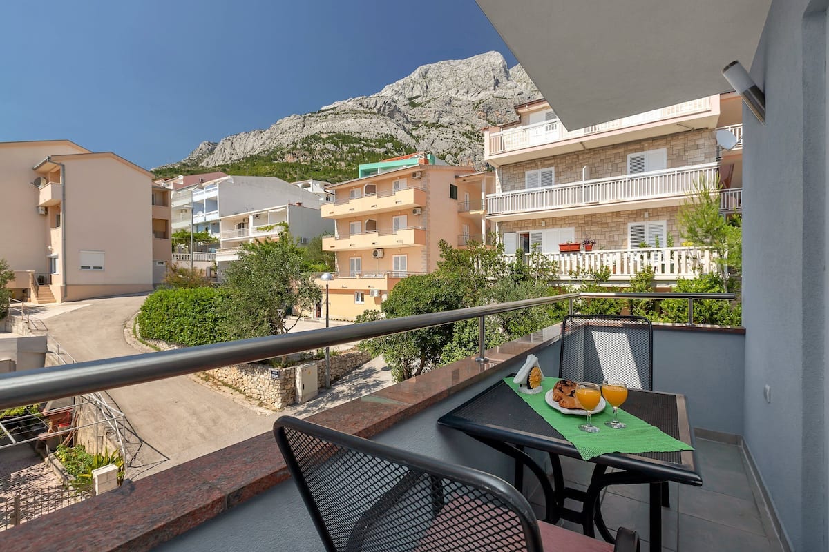 Een balkon met een ontbijttafel, met uitzicht op een straat en gebouwen, met een berg op de achtergrond.