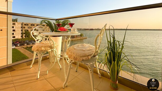 A balcony with a table set for two, overlooking a body of water.
