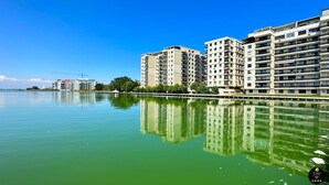 A waterfront residential area with multi-story buildings, a clear sky, and calm water reflecting the buildings.