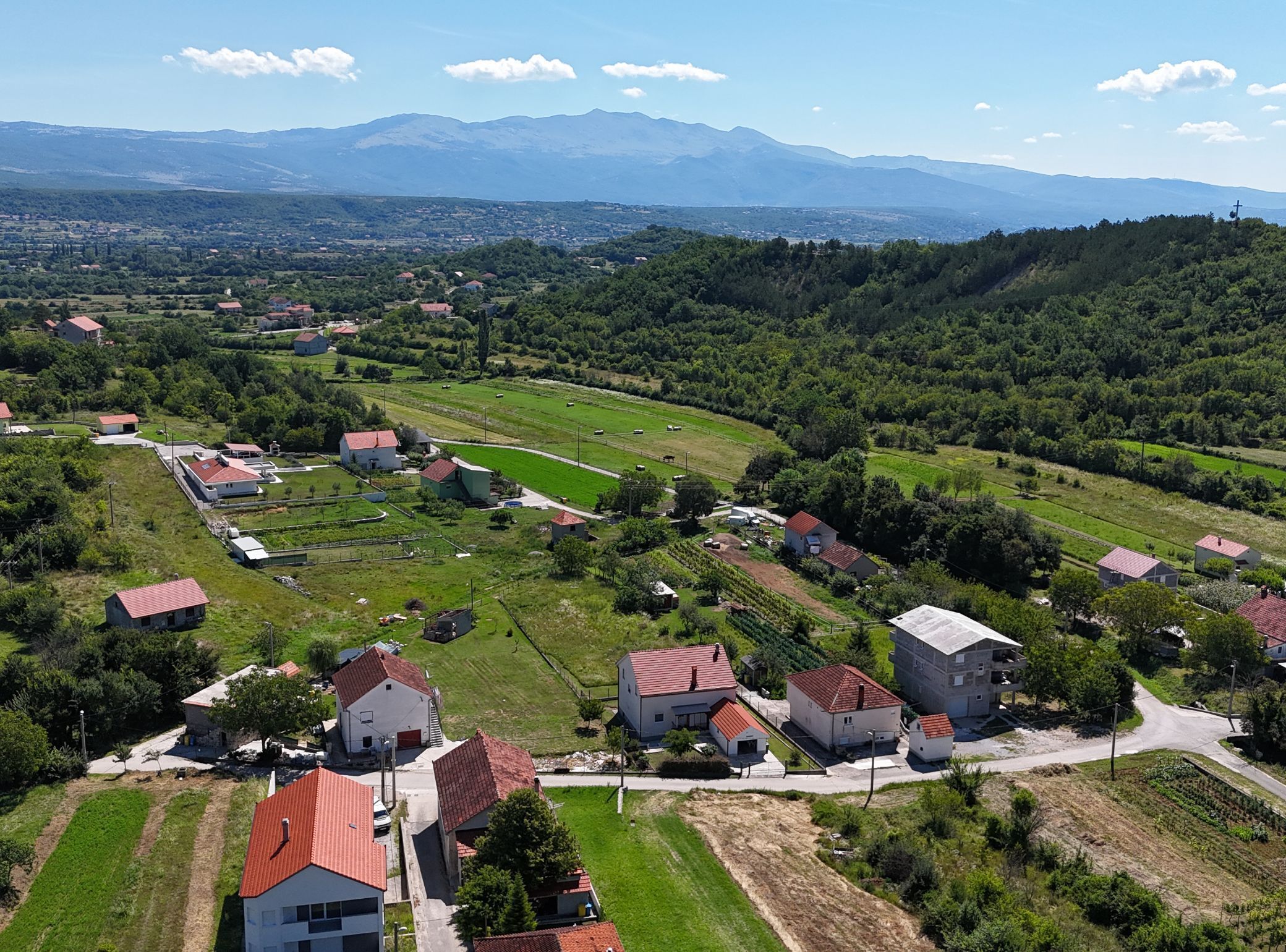 Vue aérienne d’un village rural, avec des maisons, des champs et des montagnes en arrière-plan.