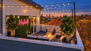 A rooftop terrace with outdoor seating, a neon sign, and a cityscape view.