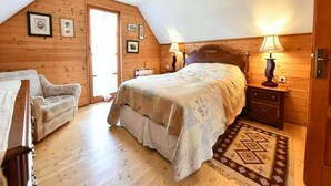 A cozy bedroom with a wooden ceiling, a bed with a floral bedspread, a nightstand with a lamp, and a chair. - Tetina Kuća (Saborsko)
