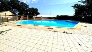 A rectangular swimming pool with a tiled deck, surrounded by trees and a building in the background. - Vacations in Corsica (Santa-Maria-Poggio)