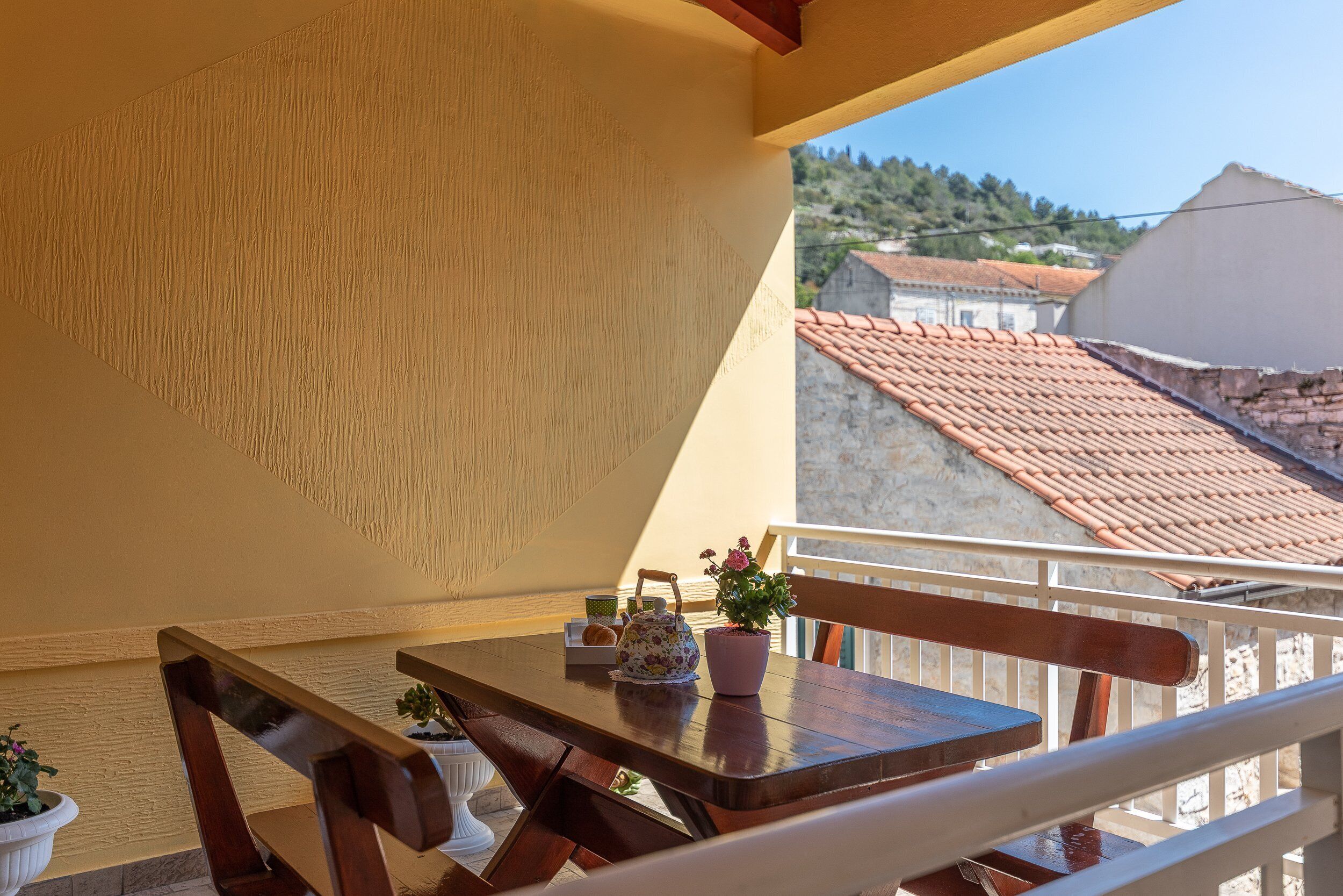 A balcony with a wooden table, a potted plant, and a teapot.
