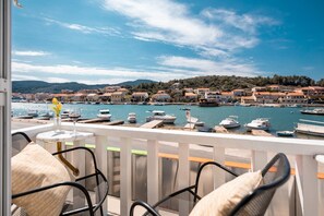 Un balcon agrémenté de fauteuils et d’une table en osier, offrant une vue sur une marina avec des bateaux et une ville côtière.