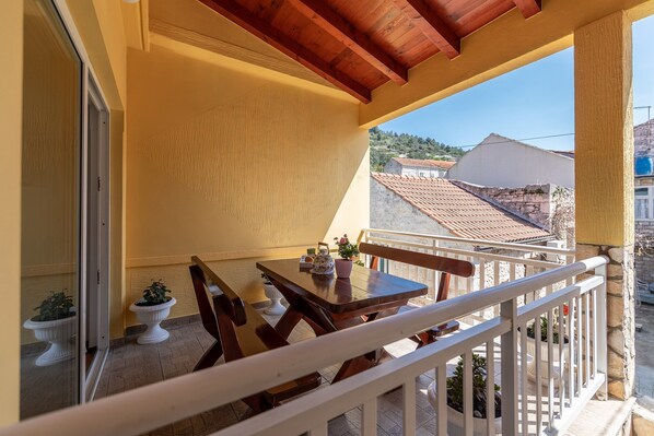 En balkon med et træbord og stole, plantekrukker og udsigt til bygninger i baggrunden.