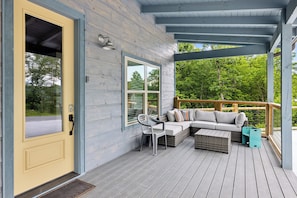 A wooden deck with a sofa and chairs, a door, and a window.