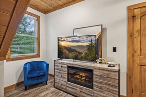 Uma sala de estar moderna com lareira, televisão montada acima e uma poltrona azul.