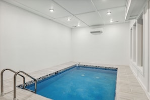 Piscina com borda azulejada, escada de metal e unidade de ar condicionado no teto.