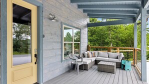 A wooden deck with a sofa and chairs, a door, and a window. - Luxury Cabin|Indoor Pool|Hot Tub|Ping Pong (Sevierville)