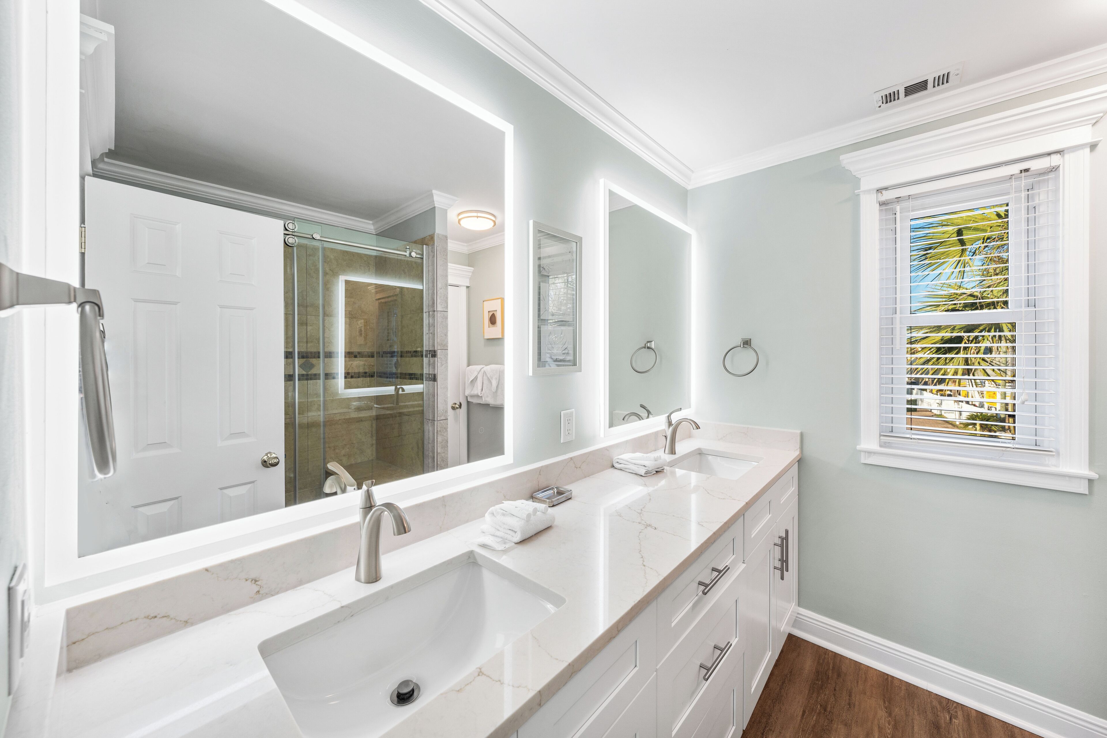 A bathroom with a double sink vanity, a large mirror, and a window with blinds.