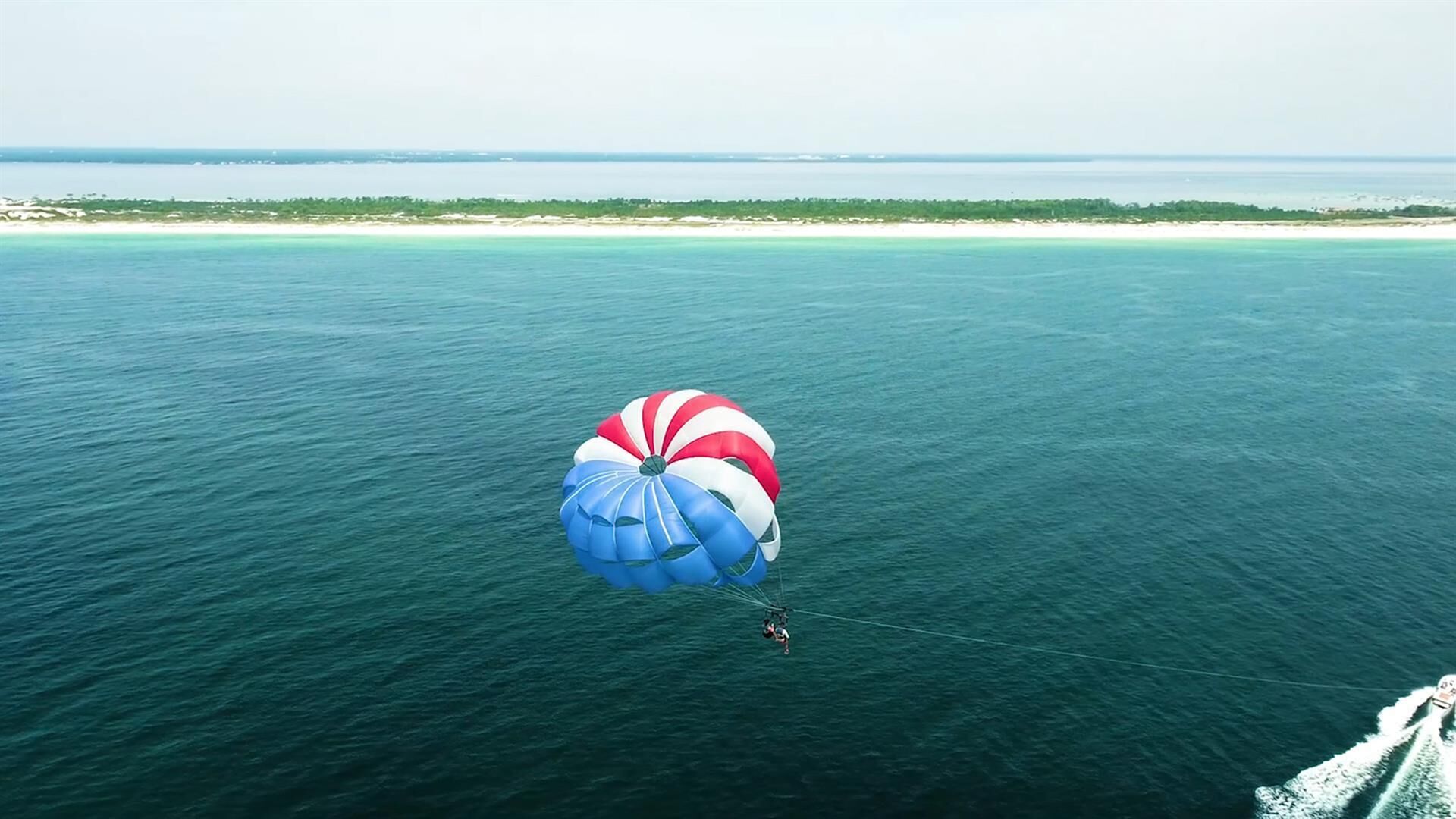 Una persona practica parasailing sobre una extensa masa de agua, con una vista despejada de la costa lejana.