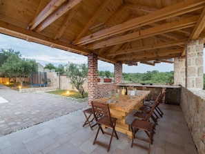 An outdoor patio with a wooden table and chairs, a brick chimney, and a stone wall. - Apartments Mistral (Razanac)