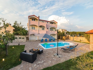 A two-story building with a swimming pool, outdoor seating, and a stone wall. - Apartments Mistral (Razanac)