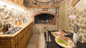 Eine rustikale Küche mit Steinwand, Holzschränken, einem Backofen aus Ziegeln und einem Essbereich mit gedecktem Tisch.