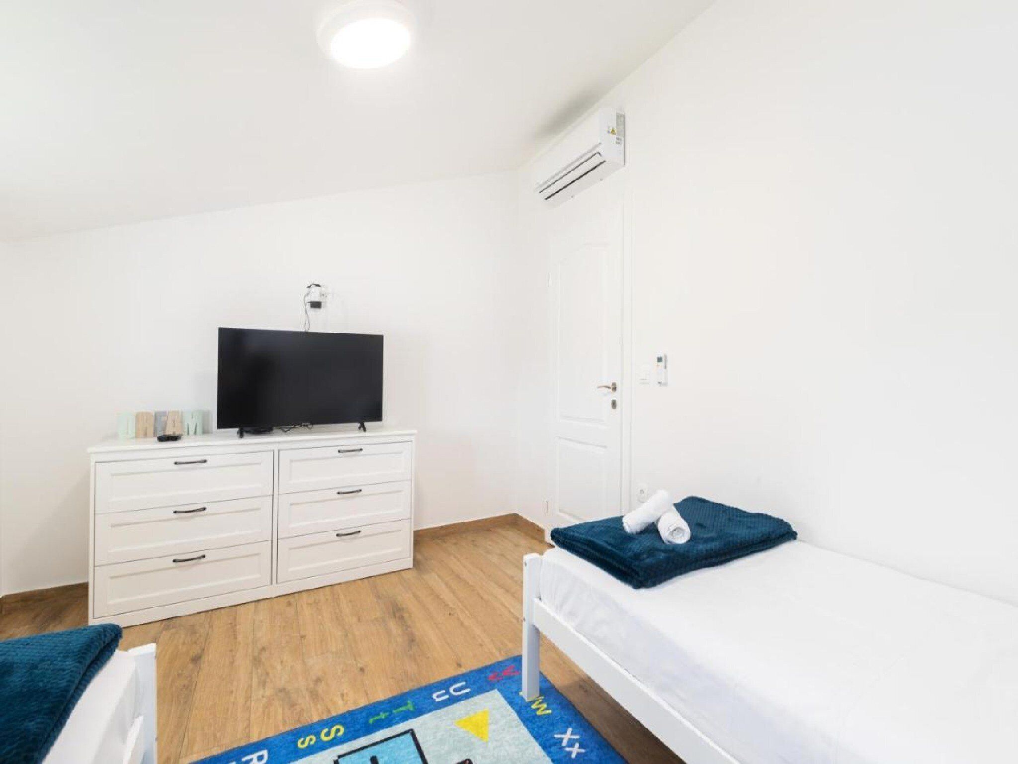 Quarto com uma cama de solteiro, uma televisão sobre um penteadeira e um guarda-roupa branco.