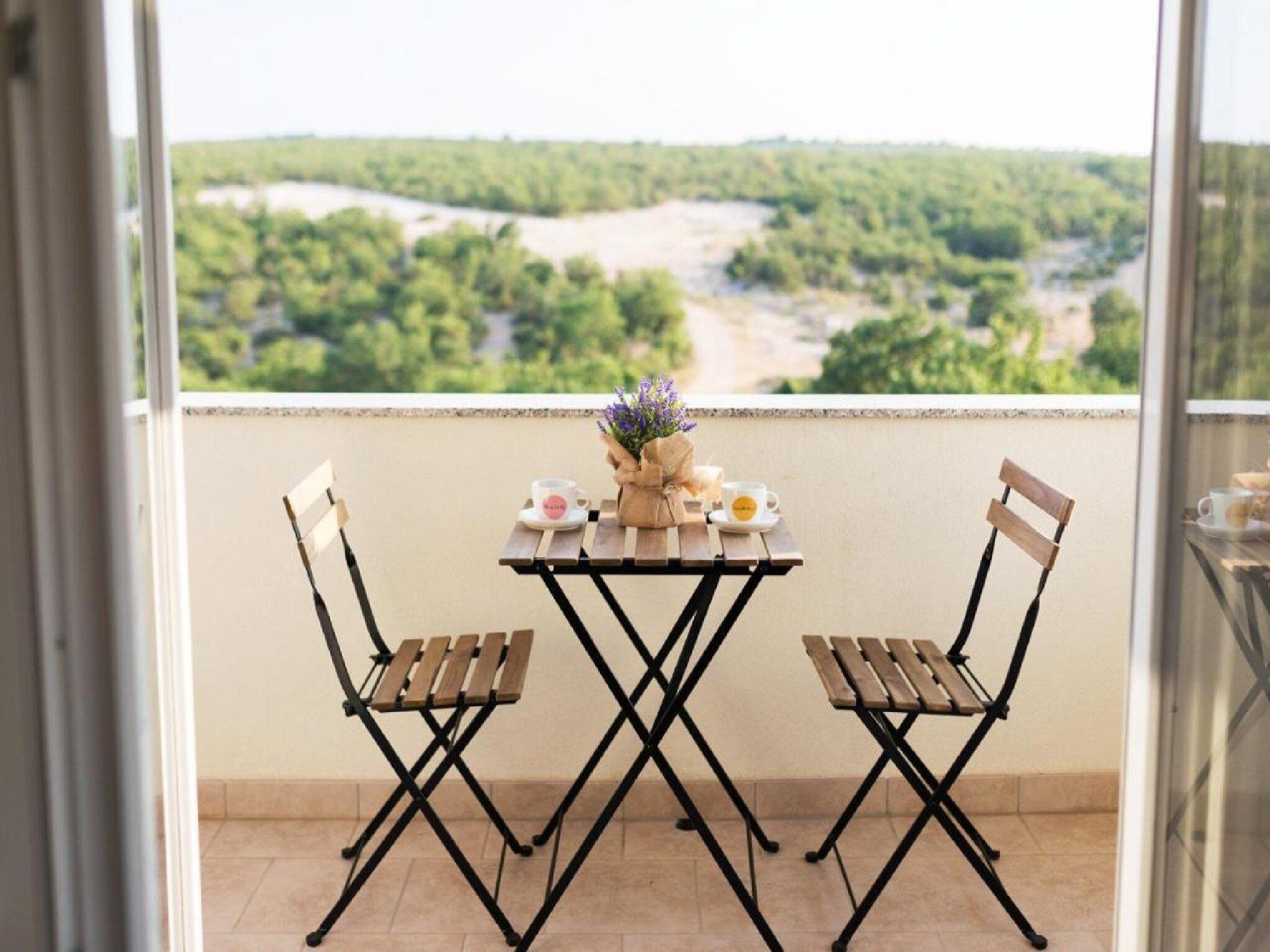 Ein Balkon mit Tisch für zwei Personen, eine Blumenvase und zwei Tassen.