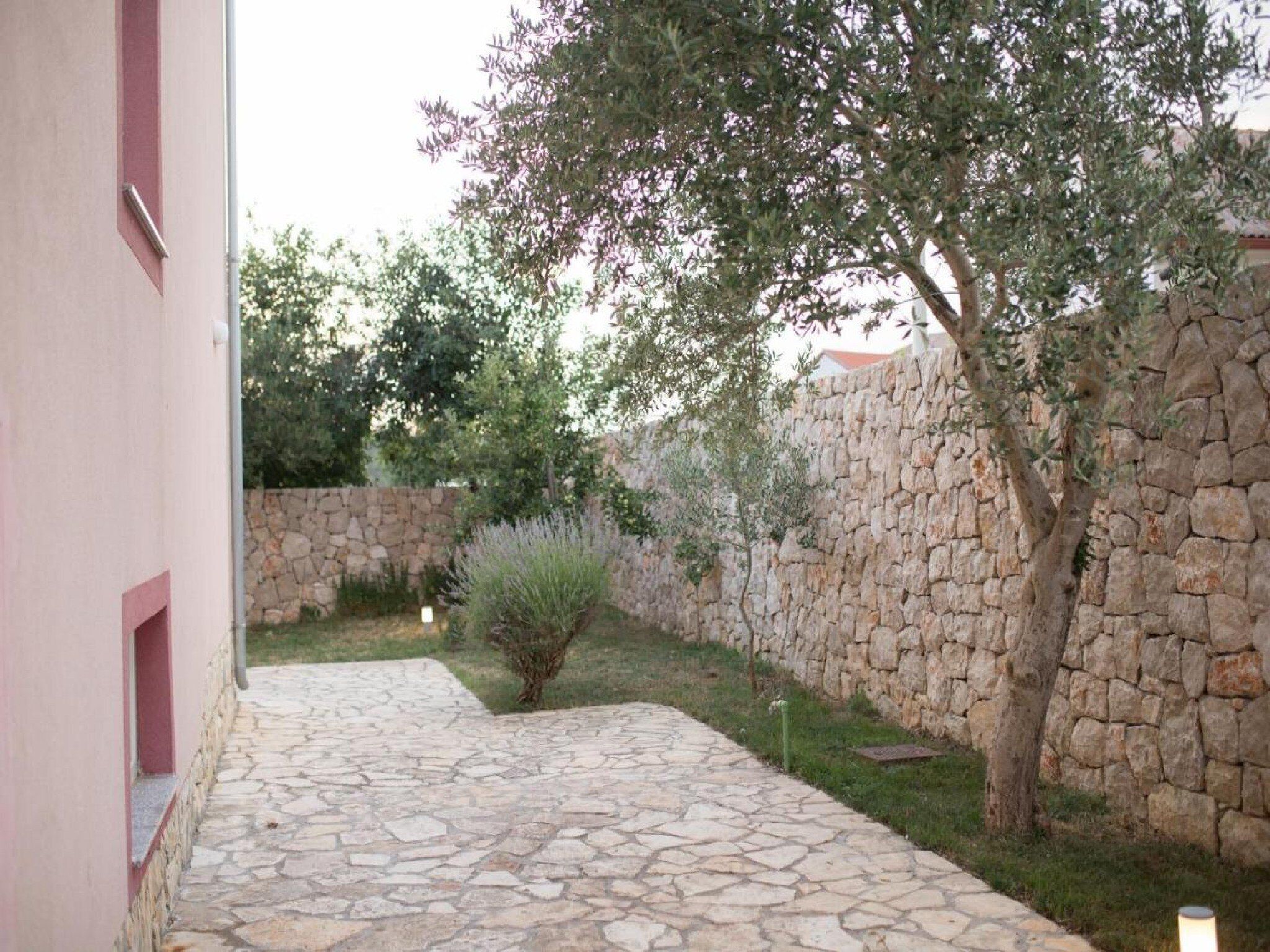 A stone pathway leading to a stone wall with a tree and shrubbery.