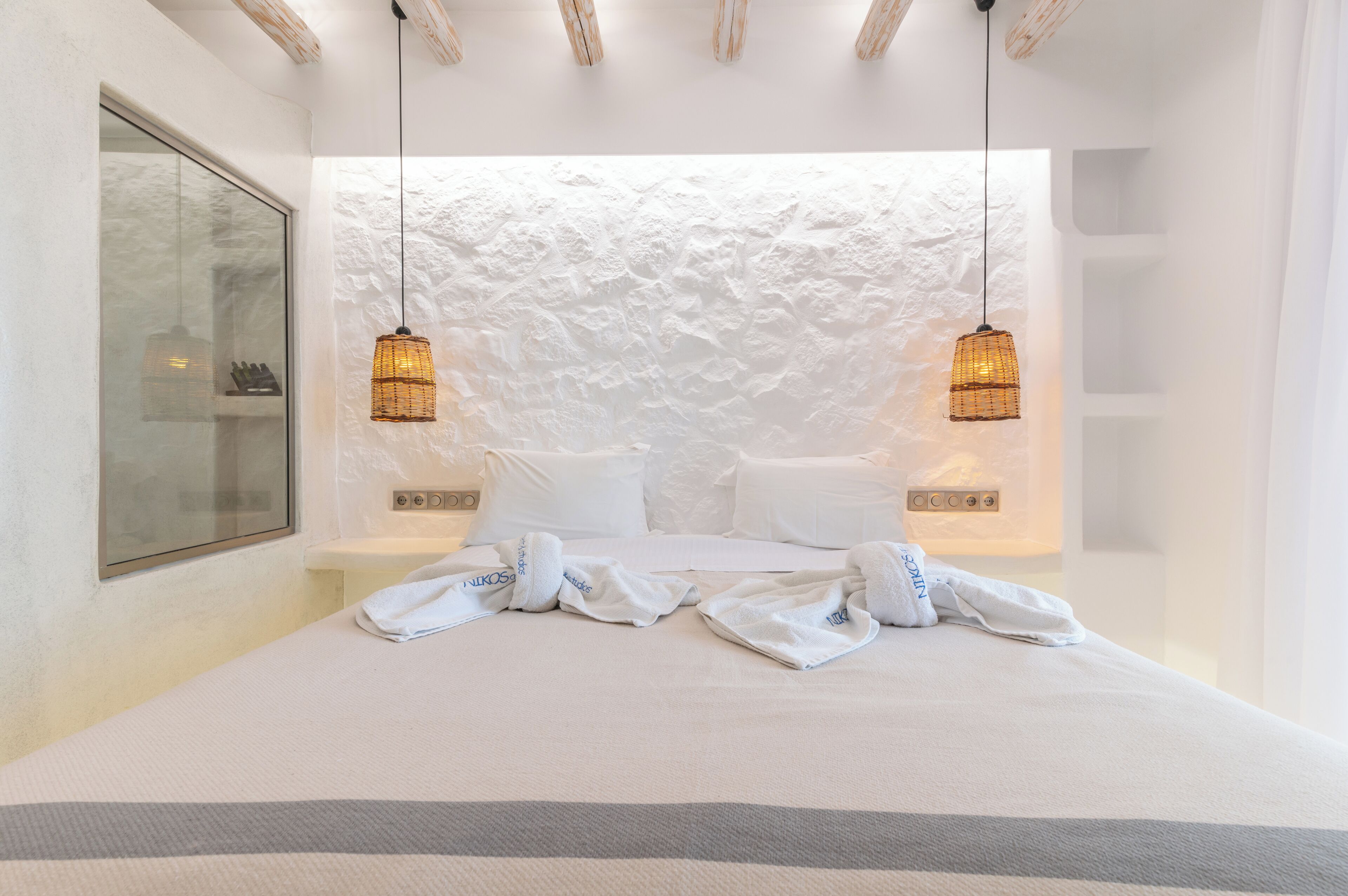 A hotel room with a large bed, two bedside tables, a white textured wall, and two hanging lamps.