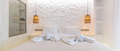 A hotel room with a large bed, two bedside tables, a white textured wall, and two hanging lamps.