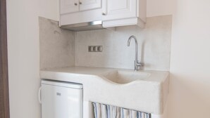 A compact kitchen with white cabinets, a built-in dishwasher, and a striped curtain. - Nikos Apartments & Studios (Naxos)