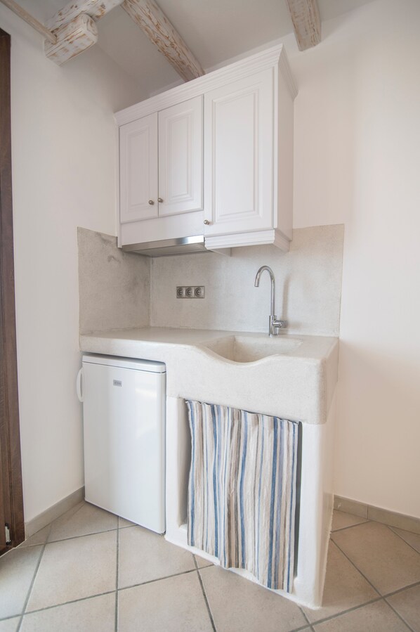 A compact kitchen with white cabinets, a built-in dishwasher, and a striped curtain.