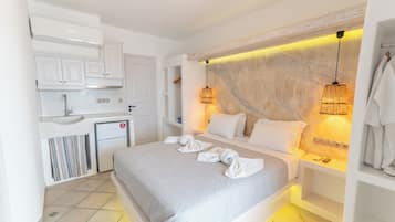 A modern hotel room with a bed, bedside tables, a small kitchenette, and a bathroom.
