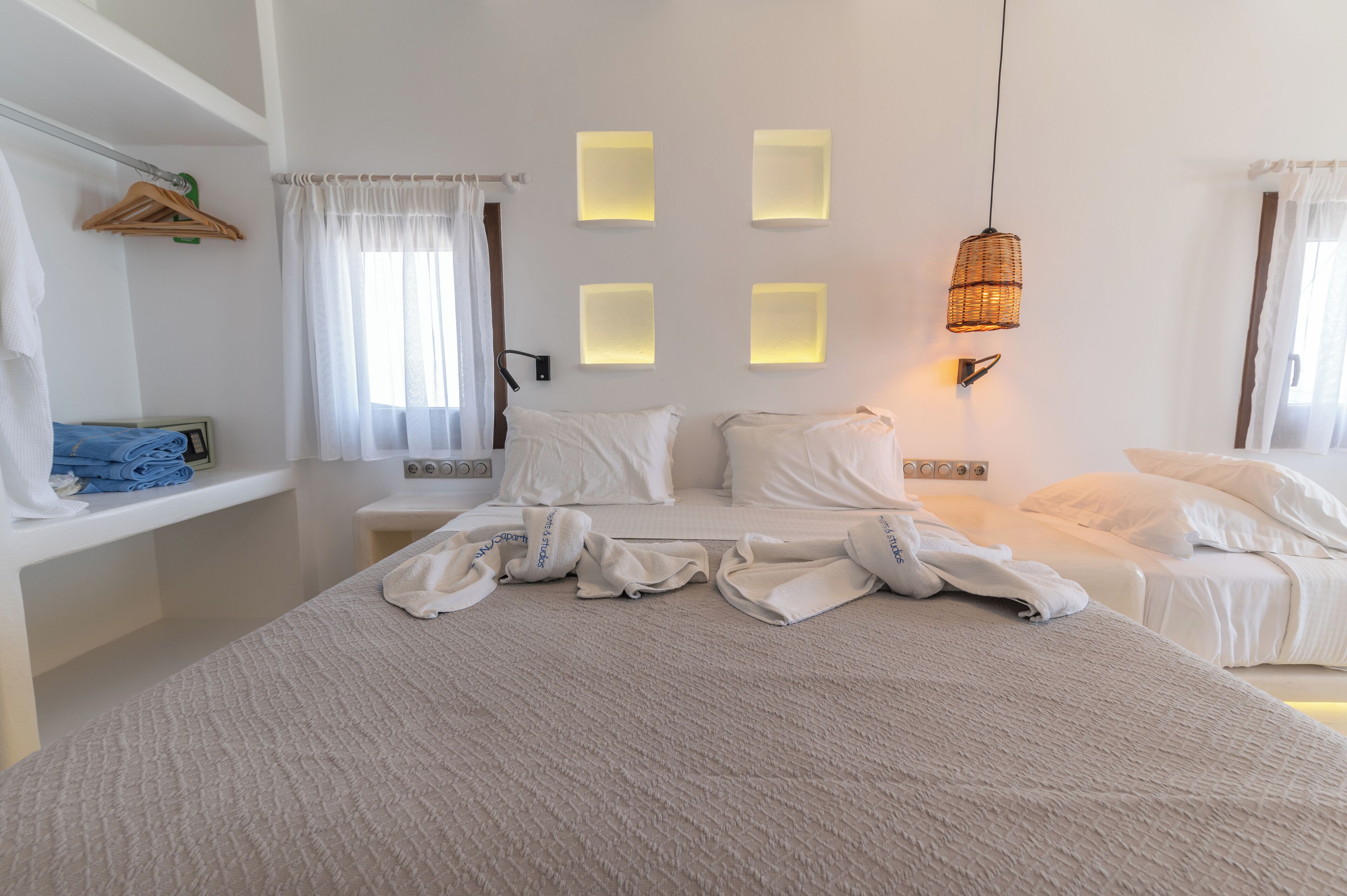 A hotel room with a bed, bedside tables, a hanging light fixture, and a window with curtains.
