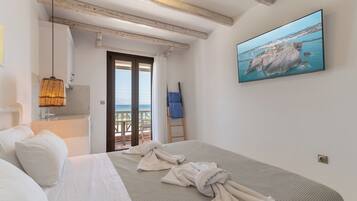 A hotel room with a bed, a painting of a coastal scene, a balcony with a view, and a wooden ceiling.