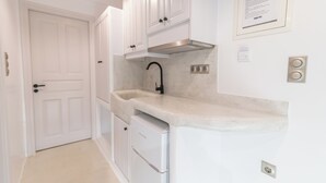A compact kitchen with white cabinetry, a stainless steel range hood, and a built-in sink. - Nikos Apartments & Studios (Naxos)