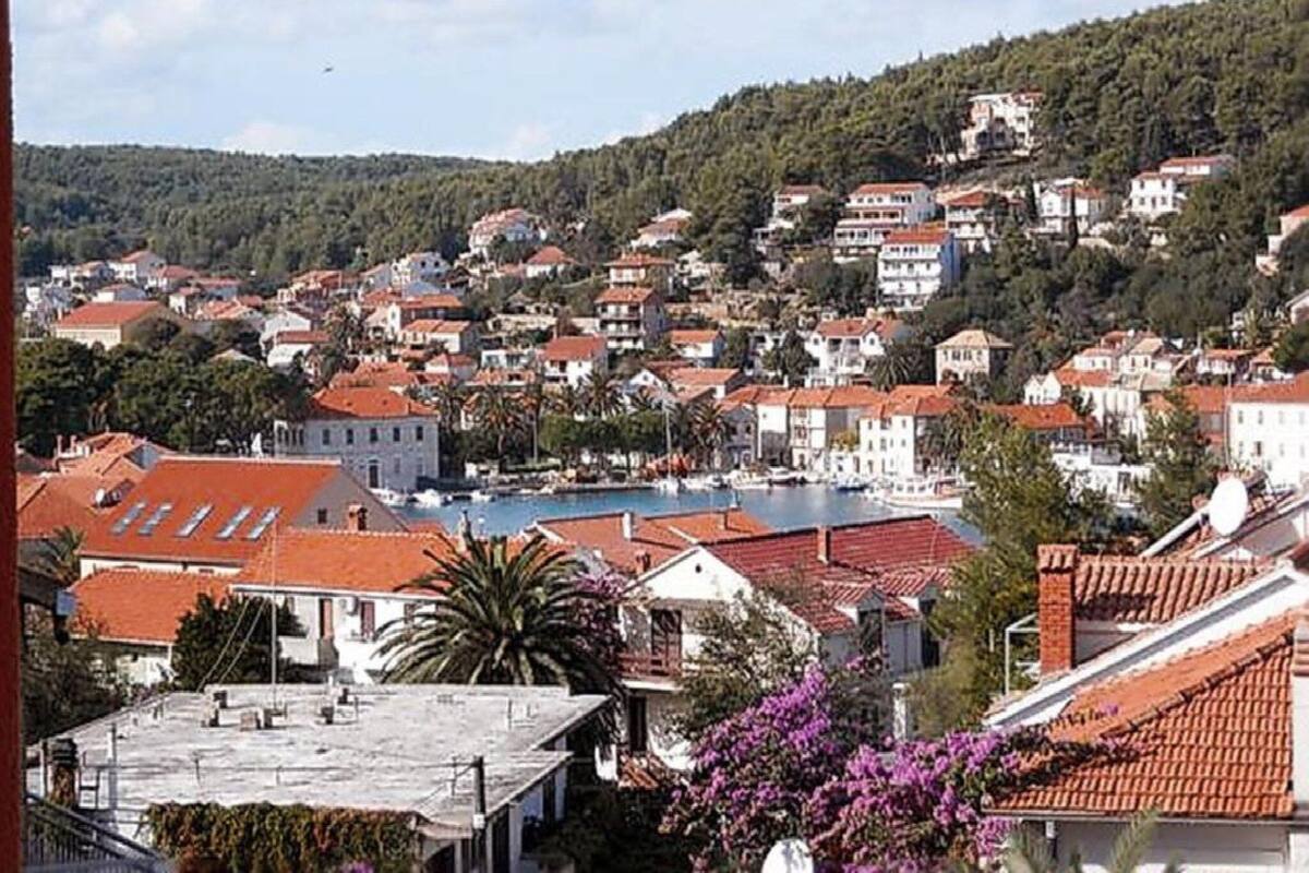 A coastal town with terracotta-roofed buildings, a marina, and a hillside backdrop.