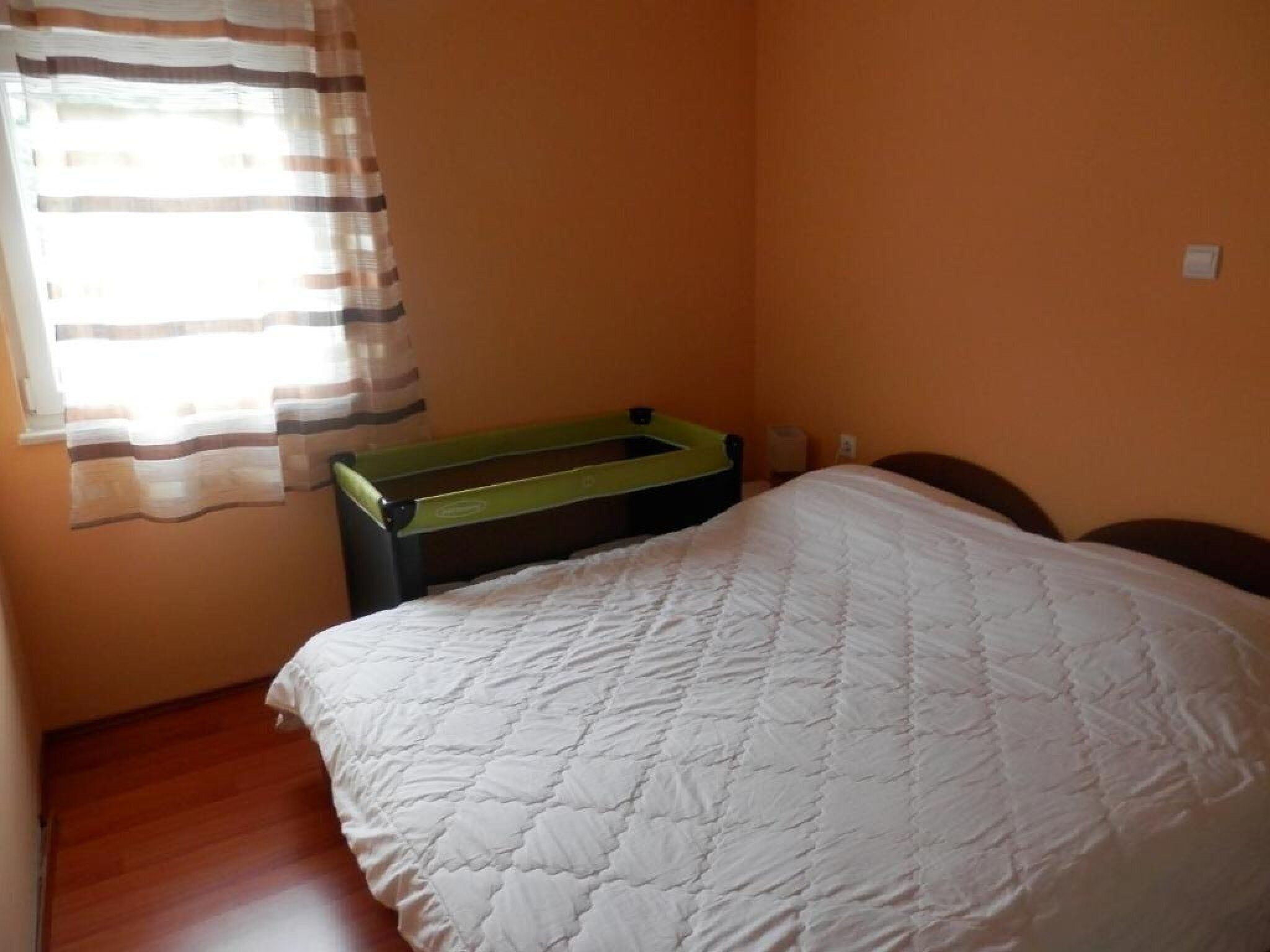 A small, simple room with a bed, a bench, and a window with curtains.