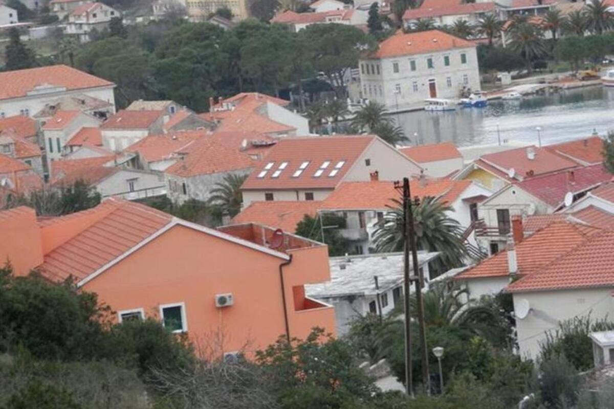 A residential area with closely packed houses, some with red-tiled roofs, and a body of water in the background.