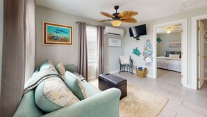 A living room with a sofa, a coffee table, a ceiling fan, a TV, and a painting on the wall. - Private Pool, Golf Cart Access, Boat Parking (Port Aransas)