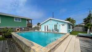 A backyard with a swimming pool, a wooden deck, and a small blue house with a door and windows. - Private Pool, Golf Cart Access, Boat Parking (Port Aransas)