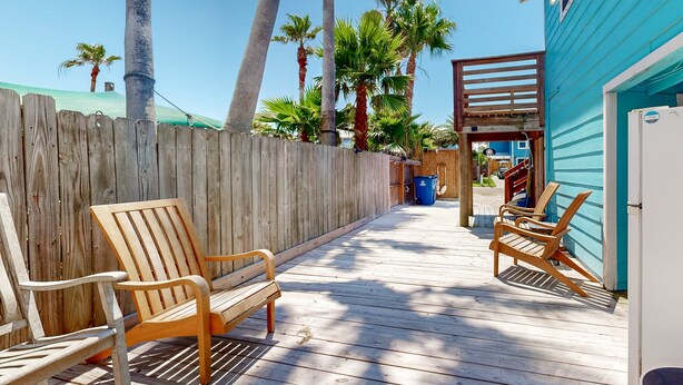 A wooden deck with chairs and a bench, a wooden fence, and a building with a blue exterior. - Private Pool, Golf Cart Access, Boat Parking (Port Aransas)