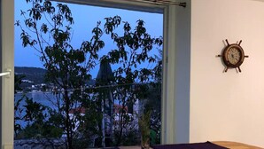 A room with a wooden table and two white chairs, a window with a view of a cityscape, and a ship's wheel on the wall. - Seafront House Antonia (Rogoznica)