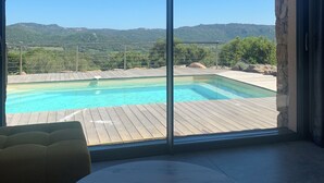 A room with a large sliding glass door leading to a pool area with a view of mountains. - Cozy villa between sea and mountains (Figari)