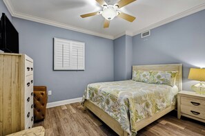 A bedroom with a bed, a nightstand, a lamp, a ceiling fan, a wardrobe, and a window with shutters.