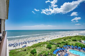 A beach resort with a pool, beach umbrellas, and a view of the ocean.