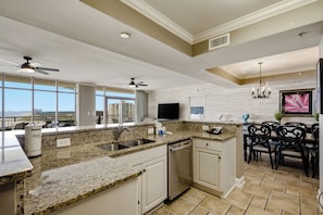 A modern kitchen with granite countertops, a dishwasher, and a dining area with black chairs.