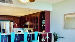 A dining area with a glass table, four grey chairs, a ceiling fan, and wooden cabinets.