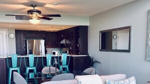 A modern living room with a grey sofa, teal chairs, a glass dining table, and a ceiling fan.