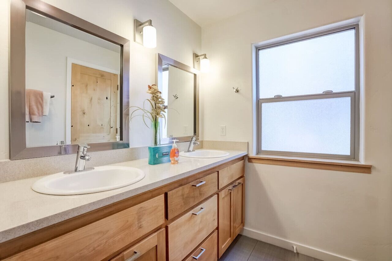 Un baño con dos lavamanos, armarios de madera, un espejo grande y una ventana.