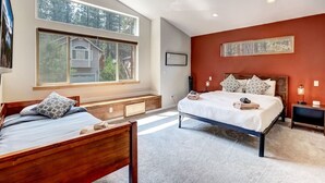 Un dormitorio con dos camas de madera, ventanas amplias, un ventilador de techo y una pared de acento roja.