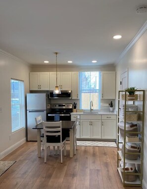 A modern kitchen with white cabinets, a stainless steel refrigerator, an oven, a sink, and a dining area with a table and chairs.