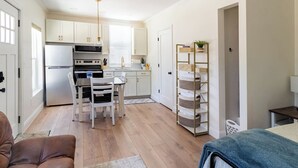 A modern kitchen with white cabinets, a stainless steel refrigerator, and a dining area with a table and chairs. - Private Urban Cottage in Denver’s RiNo District (Denver)