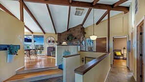 Un interior espaiós amb una escala de fusta, una zona de menjador amb vistes i un espai d'estar acollidor amb un coixí groc.